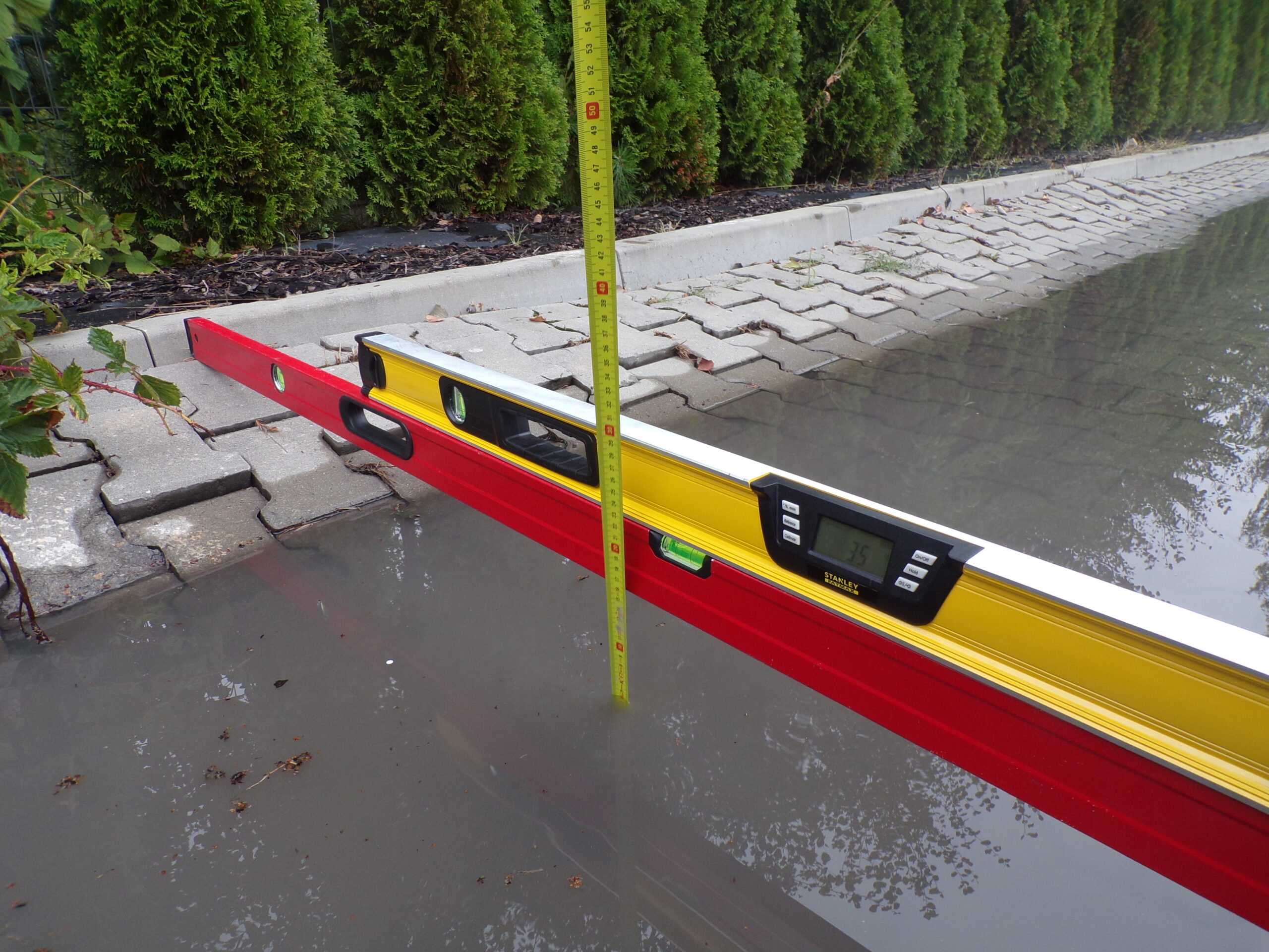 Ekspert budowlany dokonuje pomiaru deformacji kostki brukowej za pomocą poziomnicy i niwelatora w celu oceny nierówności oraz jakości wykonania nawierzchni.