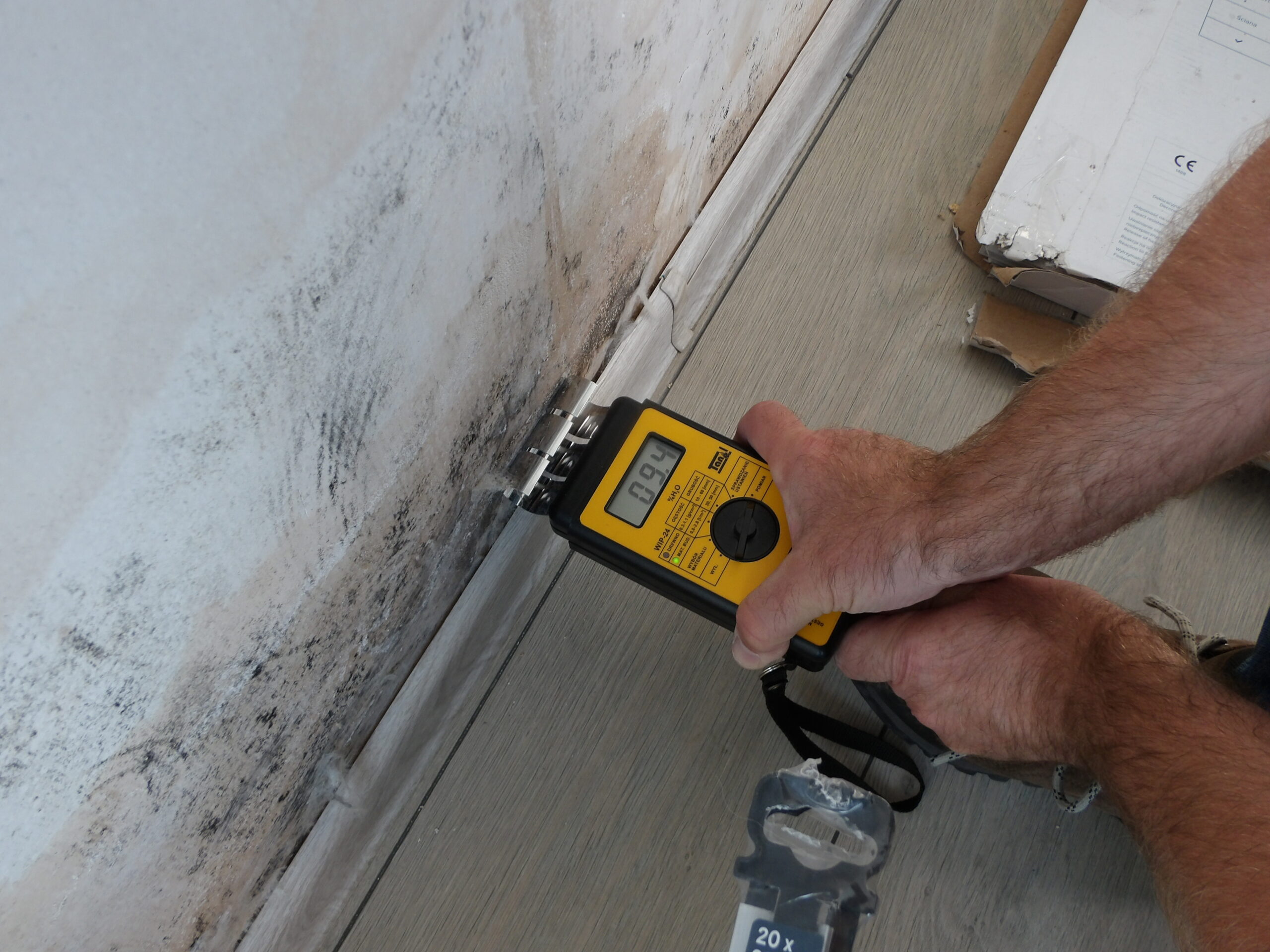 Ekspert budowlany dokonuje pomiaru wilgotności ściany przy użyciu specjalistycznego miernika w celu oceny problemów związanych z zawilgoceniem budynku.