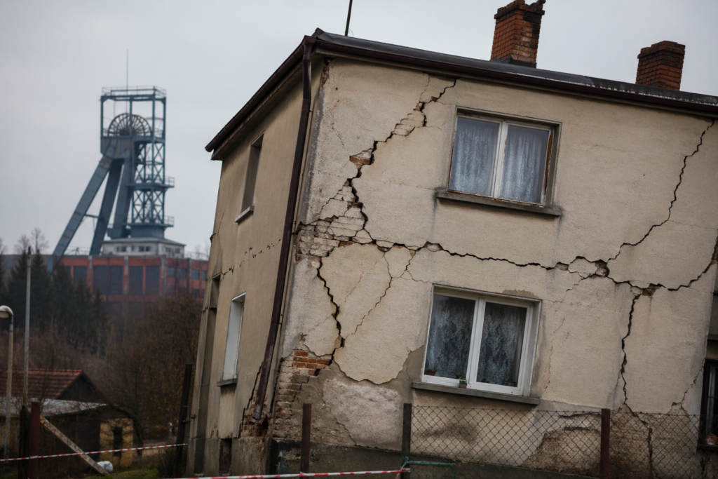 Pękające ściany budynku i wychylenie konstrukcji spowodowane szkodami górniczymi, szyb kopalni w tle